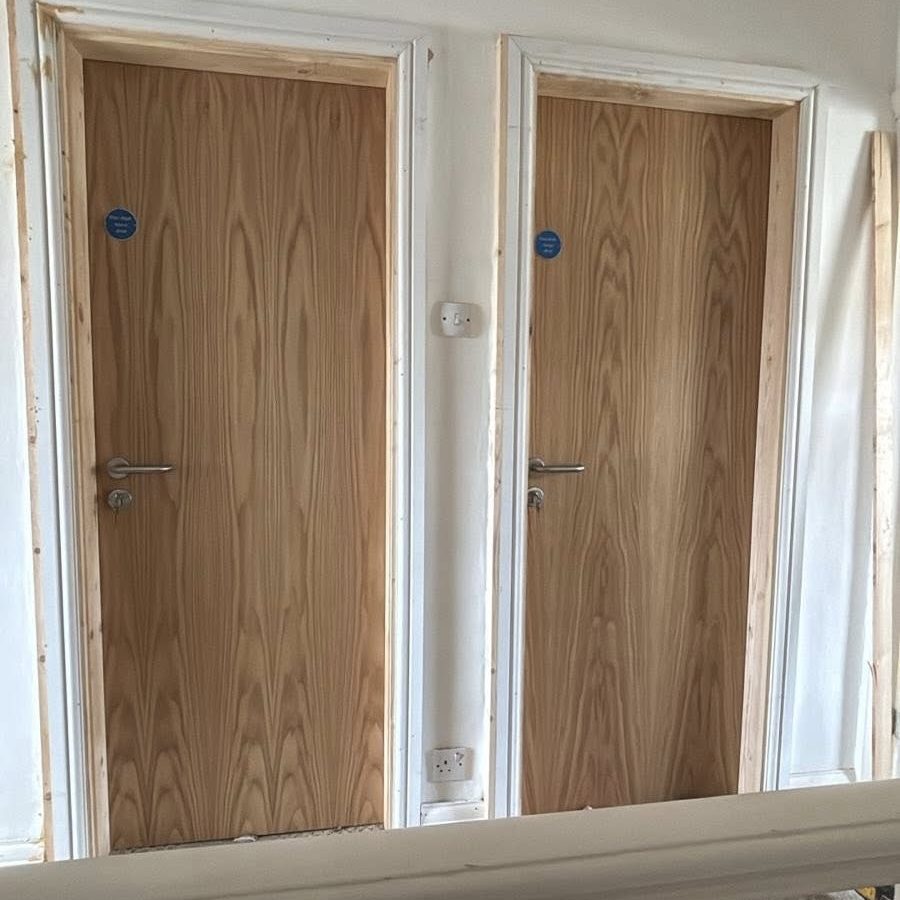 Pair of newly installed timber fire doors in frames with statutory safety signage, showcasing our complete supply and fit service across the