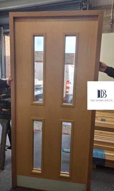 A timber veneer fire door with four rectangular glazed vision panels and a protective metal kick plate.