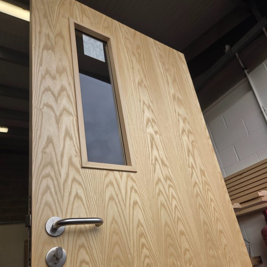 Bespoke internal ash fire door featuring a natural grain finish and a vertical vision panel for commercial visibility.
