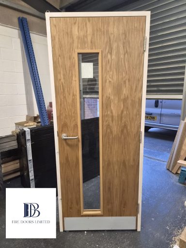European oak veneer fire doorset in a primed frame featuring a narrow glazed vision panel, kick plate, and lever handle