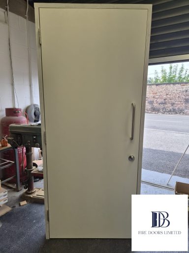 White Formica laminate fire door set in a primed frame fitted with stainless steel D-pull handle and deadlock