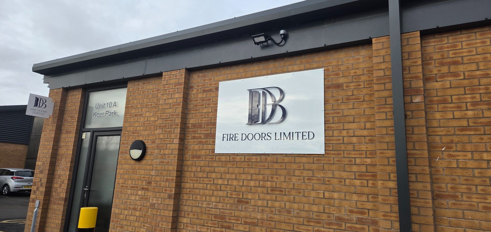 Exterior view of the DB Fire Doors Limited workshop at Unit 10A Keer Park, Carnforth featuring a large company logo sign on a brick building