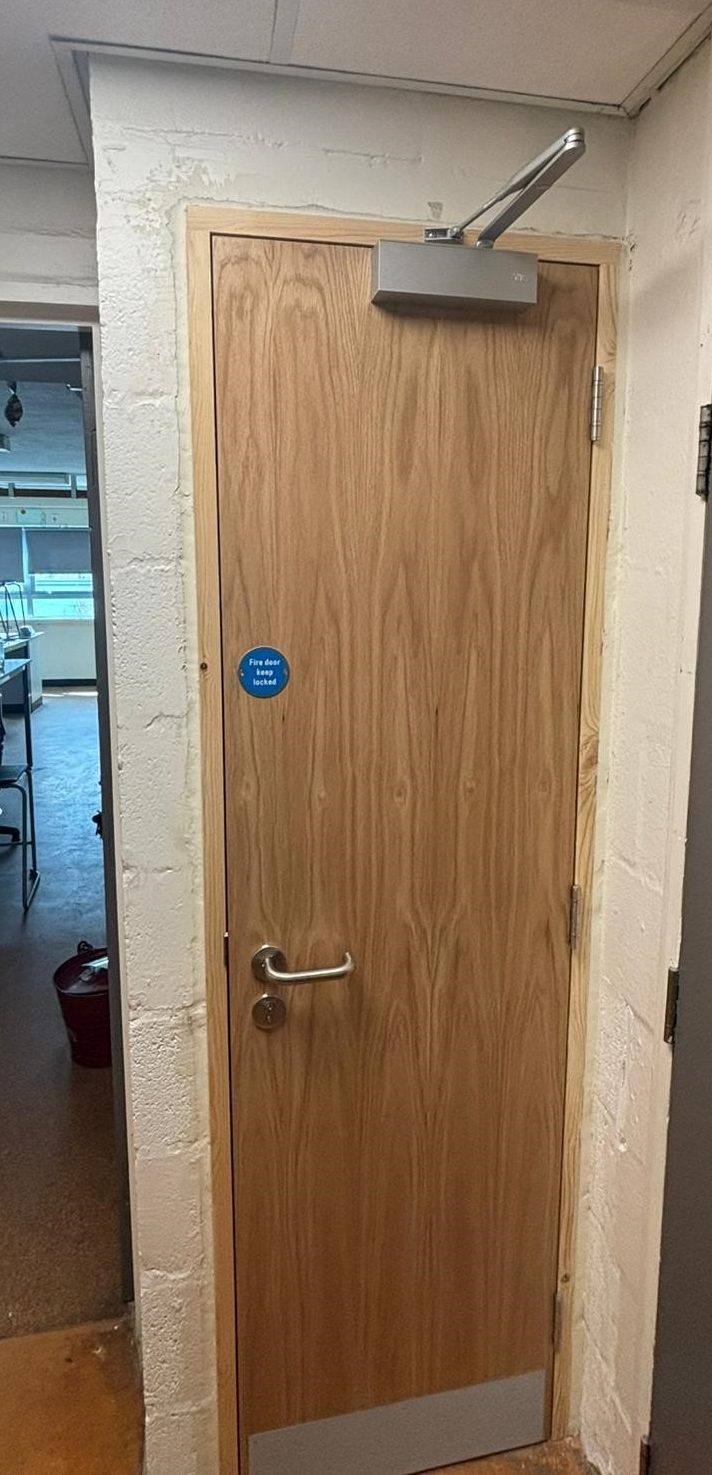 Commercial Fire Door Supply and Fit Flush commercial timber fire door fitted with overhead closer and safety signage, manufactured and installed in Lancashire.